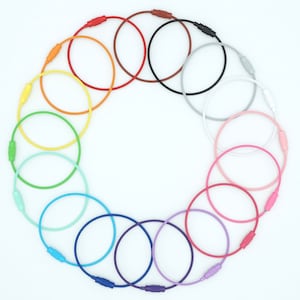 May include: A set of 18 colourful keyrings arranged in a circle. The keyrings are made of a flexible, durable material and feature a variety of bright colours, including red, orange, yellow, green, blue, purple, pink, and white.