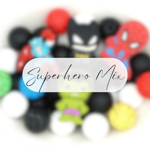 May include: A collection of silicone beads in various colours including black, white, red, yellow, blue, and green, featuring shaped beads of superhero characters and round beads. The text Superhero Mix is overlaid in the centre of the image.