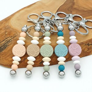 May include: Five colourful beaded keychains with a floral charm and a silver key ring. Each keychain has a different colour scheme, including peach, beige, green, blue, and purple.