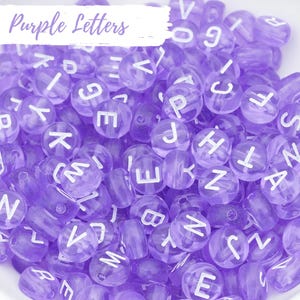 May include: A close-up of a collection of purple letter beads. The beads are made of translucent plastic and have white letters on them. The letters are all different and are arranged in a random order.