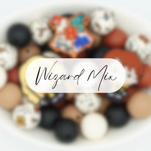 May include: A selection of colourful beads in a white bowl. The beads are various sizes and colours, including black, white, brown, and orange. A star-shaped bead with a crest design is visible. The text "Wizard Mix" is overlaid on the image.