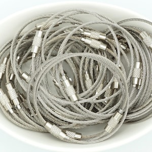 May include: A close-up of a bowl filled with silver metal keychains. The keychains are made of a braided cable with silver metal clasps.