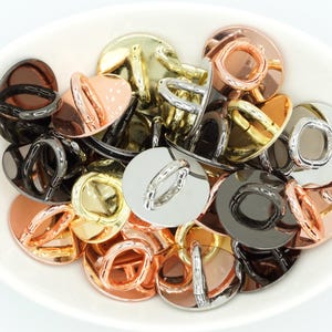 Könnte beinhalten: Eine Sammlung runder Metallringe mit verschiedenen Oberflächen, darunter Gold, Silber und Schwarz. Die Ringe sind in einer Schüssel angeordnet und bereit für Bastelprojekte.