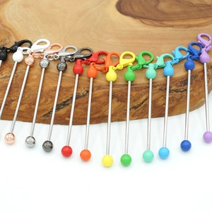 May include: A set of 14 colourful metal keychains with a silver metal rod and a small ball at the end. The balls are in various colours, including black, white, copper, red, orange, yellow, green, blue, and purple.