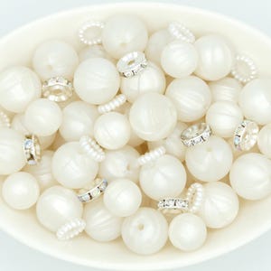 May include: A white bowl filled with white pearl-like beads and silver-toned bead caps with clear rhinestones.