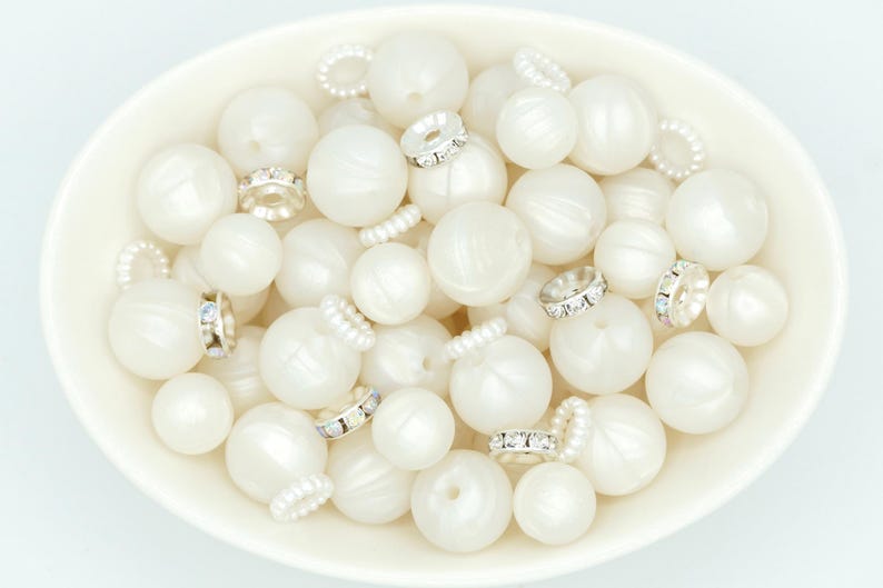 May include: A white bowl filled with white pearl-like beads and silver-toned bead caps with clear rhinestones.