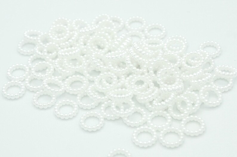 May include: A large pile of white pearl rings. The rings are made of small, round pearls that are strung together to form a circle.