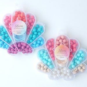 May include: A set of silicone beads in a seashell-shaped container. The beads are in four colours: pink, blue, light brown, and white. The container has a label that says "Silicone DIY Bracelet Kit".