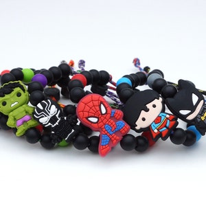 Peut inclure: Un ensemble de six bracelets de personnages de super-héros avec des perles noires et des breloques de personnages colorés. Les personnages incluent Hulk, Spiderman, Superman, Batman, Thor et Black Panther.