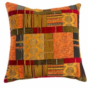 May include: A square throw pillow featuring a patchwork design of various fabric textures in shades of orange, red, olive green, and dark brown. The surface displays repeating spiral patterns, horizontal stripes, and visible decorative stitching.