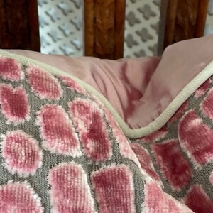 May include: Close-up of a pink and grey patterned throw pillow with a white piping trim. The pillow is made of a soft, plush fabric.