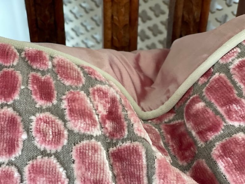 May include: Close-up of a pink and grey patterned throw pillow with a white piping trim. The pillow is made of a soft, plush fabric.