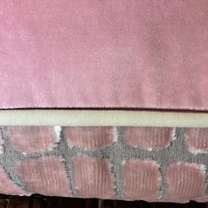May include: A pink velvet cushion with a white trim and a patterned back. The back of the cushion features a repeating pattern of pink circles on a grey background.