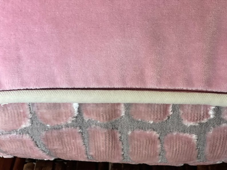 May include: A pink velvet cushion with a white trim and a patterned back. The back of the cushion features a repeating pattern of pink circles on a grey background.