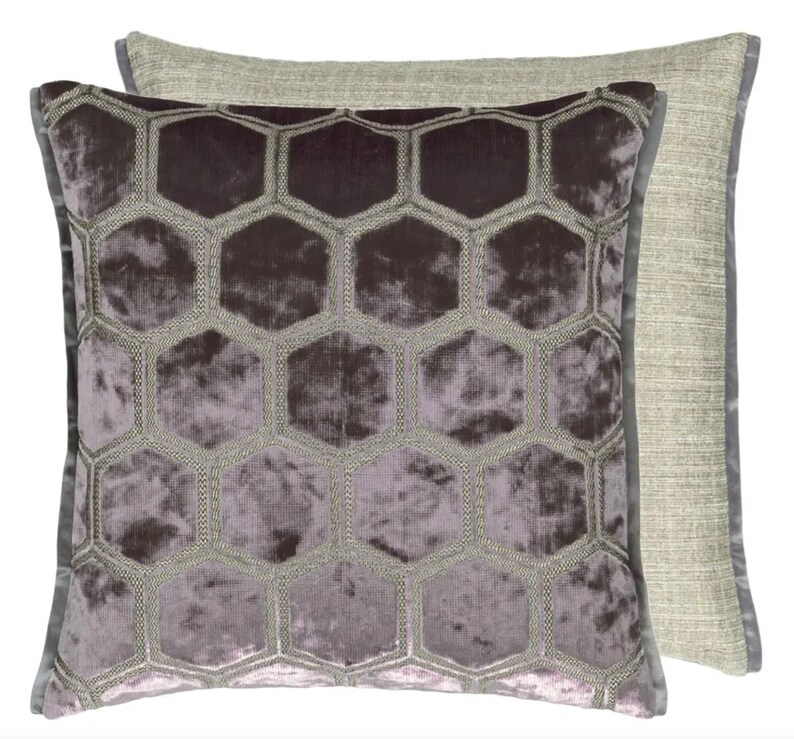 May include: A square throw pillow with a geometric pattern of hexagons. The pillow is made of a soft, plush fabric with a subtle sheen. The hexagons are embroidered in a contrasting color, creating a raised texture. The pillow has a light gray backing.