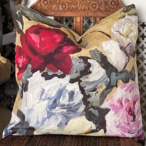 Peut inclure: Un coussin décoratif avec un imprimé floral représentant de grandes roses stylisées dans des tons de rouge, rose, blanc et bleu sur un fond de lin beige.