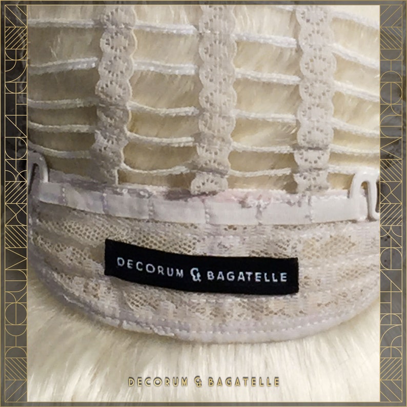 May include: Close-up of the interior of a wig, showing the construction with a lace front and adjustable straps. The wig features a light blonde color and a black label that reads "DECORUM & BAGATELLE". The bottom of the image also displays the text "DECORUM & BAGATELLE".