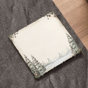 May include: A blank white card with a winter scene illustration of trees and snow. The card is on a gray textured surface.