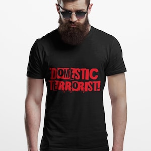 May include: Black t-shirt with the red text "DOMESTIC TERRORIST!". The shirt is worn by a person with a beard and sunglasses.