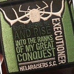 May include: A green and black embroidered patch with the text "HELARAISERS S.C. EXECUTIONER KNEEL BEFORE ME AND RISE INTO THE RANKS OF MY GREAT CONQUEST HELARAISERS S.C."