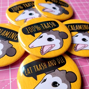 Puede incluir: Un conjunto de seis botones amarillos con un dise&ntilde;o de zarig&uuml;eya de dibujos animados. Las zarig&uuml;eyas tienen diferentes expresiones y van acompa&ntilde;adas de texto como "100% Trash", "Eat Trash and Die" y "Creaming".
