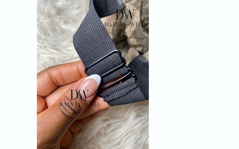 May include: Close-up of a dark gray elastic wig band with metal clips. The band is held by a hand with a French manicure. The logo "DW DAINTY WIGS" is visible in the lower left corner.