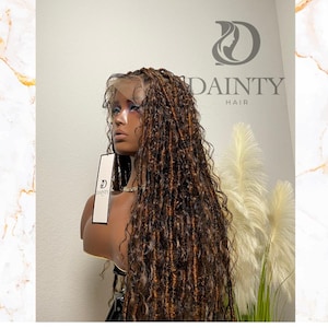 May include: A brown and blonde faux locs wig on a mannequin head. The wig has a lace front and long, flowing locs. A tag with the "DAINTY HAIR" logo hangs from the mannequin. The background is a neutral color with a marble design.