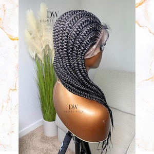 May include: A black braided wig with a lace front. The wig is styled in a box braid pattern and is on a mannequin head. The mannequin head is on a stand. The text "DSW DAINTY WIGS" is visible on the stand.