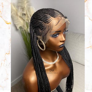 May include: A black braided wig with a lace front is displayed on a mannequin. The wig features intricate cornrow patterns and long, flowing braids. The mannequin is adorned with gold hoop earrings and a diamond necklace. The brand name "DAINTY WIGS" is visible.