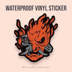 May include: A red and black vinyl sticker featuring a stylized illustration of a samurai mask with a robotic eye and flames. The text "WATERPROOF VINYL STICKER" is at the top of the image. The text "@CoreyAllenDesign" is at the bottom of the image.