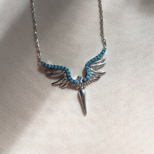 May include: A silver necklace with a turquoise stone pendant shaped like a pair of wings with a pointed tip.