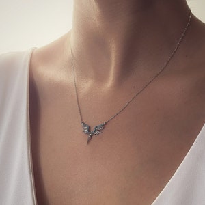 May include: A silver necklace with a delicate winged pendant featuring blue gemstones. The pendant is shaped like a pair of wings with a pointed tip.