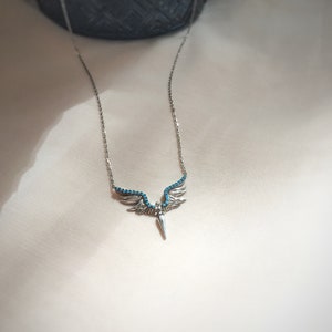 May include: A silver necklace with a turquoise angel wing pendant. The wings are detailed with small turquoise stones.