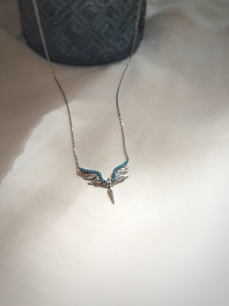May include: A silver necklace with a turquoise angel wing pendant. The wings are detailed with small turquoise stones.