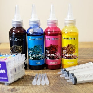 Könnte beinhalten: Vier Flaschen InkXpro-Farbsublimationsfarbe in Schwarz, Cyan, Magenta und Gelb mit Leopardenmuster. Enthält auch eine Tintenstrahlpatrone, Spritzen und Nadeln. Der Text auf den Flaschen lautet "Dye Sublimation Ink".