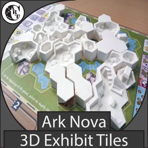 May include: White 3D exhibit tiles for the board game Ark Nova, arranged on a game board. The tiles are hexagonal and feature detailed architectural designs. The text "Ark Nova 3D Exhibit Tiles" is displayed at the bottom of the image.