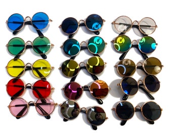 May include: A set of 12 pairs of round sunglasses with different colored lenses. The sunglasses have gold frames and are arranged in rows on a white background.