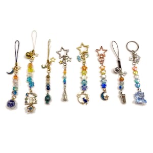 May include: A collection of eight beaded charms with various celestial and whimsical designs. Each charm features colorful beads, stars, moons, and other decorative elements. The charms are attached to keychains or phone straps, offering a decorative accessory.