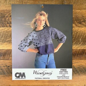 Puede incluir: Un patrón de tejido vintage para un "Puffball Sweater" de Columbia-Minerva. El patrón muestra a una mujer con un suéter azul, gris y marino con detalles de bolas. La imagen incluye el logotipo de la marca y el texto: "INSTRUCCIONES DE TEJIDO GRATUITAS con la compra de hilo Columbia-Minerva."