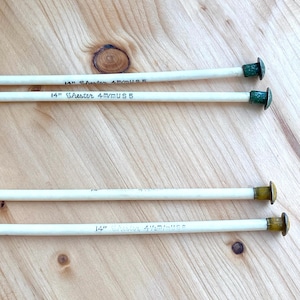 May include: Four knitting needles, each 14 inches long, with green and gold metal caps. The needles are labeled "14" Chester 4mm US 5". The needles are cream-colored and rest on a light brown wooden surface.