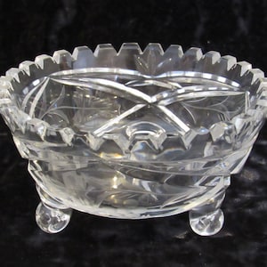 May include: A clear glass bowl with a cut glass design and three feet. The bowl is on a black background.