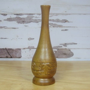 May include: A wooden vase with a carved design of palm trees. The vase is a light brown color and has a narrow neck and a wide base.