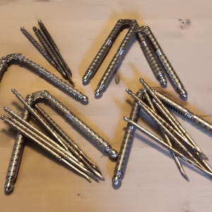May include: A collection of silver-colored nutcrackers and nut picks arranged on a light-colored wooden surface. The nutcrackers have a lever design, and the nut picks are slender and pointed.