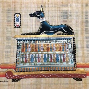 May include: An Egyptian papyrus painting featuring Anubis, the jackal-headed god, atop a decorated shrine. The artwork showcases vibrant colors and intricate details, with hieroglyphs and figures. The painting is on a textured, tan background.