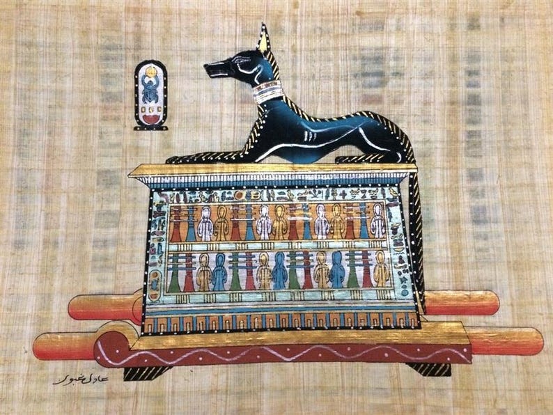 May include: An Egyptian papyrus painting featuring Anubis, the jackal-headed god, atop a decorated shrine. The artwork showcases vibrant colors and intricate details, with hieroglyphs and figures. The painting is on a textured, tan background.