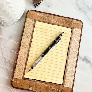May include: A wooden notepad with a yellow lined paper insert. The notepad has a cat-themed design with the text "Things to do today... probably involves cats".