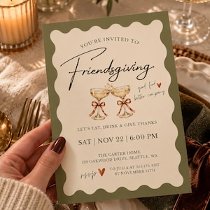 May include: A rectangular Friendsgiving invitation card with a scalloped olive green border and cream center. It features two illustrated champagne glasses with brown ribbons, text reading "You're invited to Friendsgiving," "good food, better company," "Let's eat, drink & give thanks," event details, and RSVP information.
