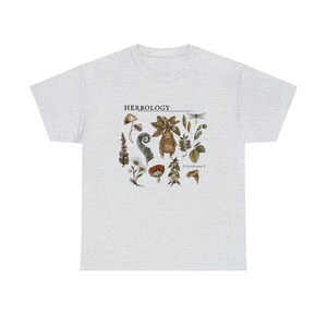 Może przedstawiać: Jasnoszary t-shirt z nadrukiem graficznym różnych roślin i grzybów. Na koszulce nadrukowany jest tekst "HERBOLOGY Greenhouse 2".