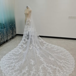 Puede incluir: Un velo de novia blanco con delicado bordado de encaje floral. El velo es largo y fluido, con un borde festoneado.