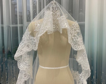 May include: A white bridal veil with a delicate lace trim and beaded embellishments. The veil is draped over a dress form.